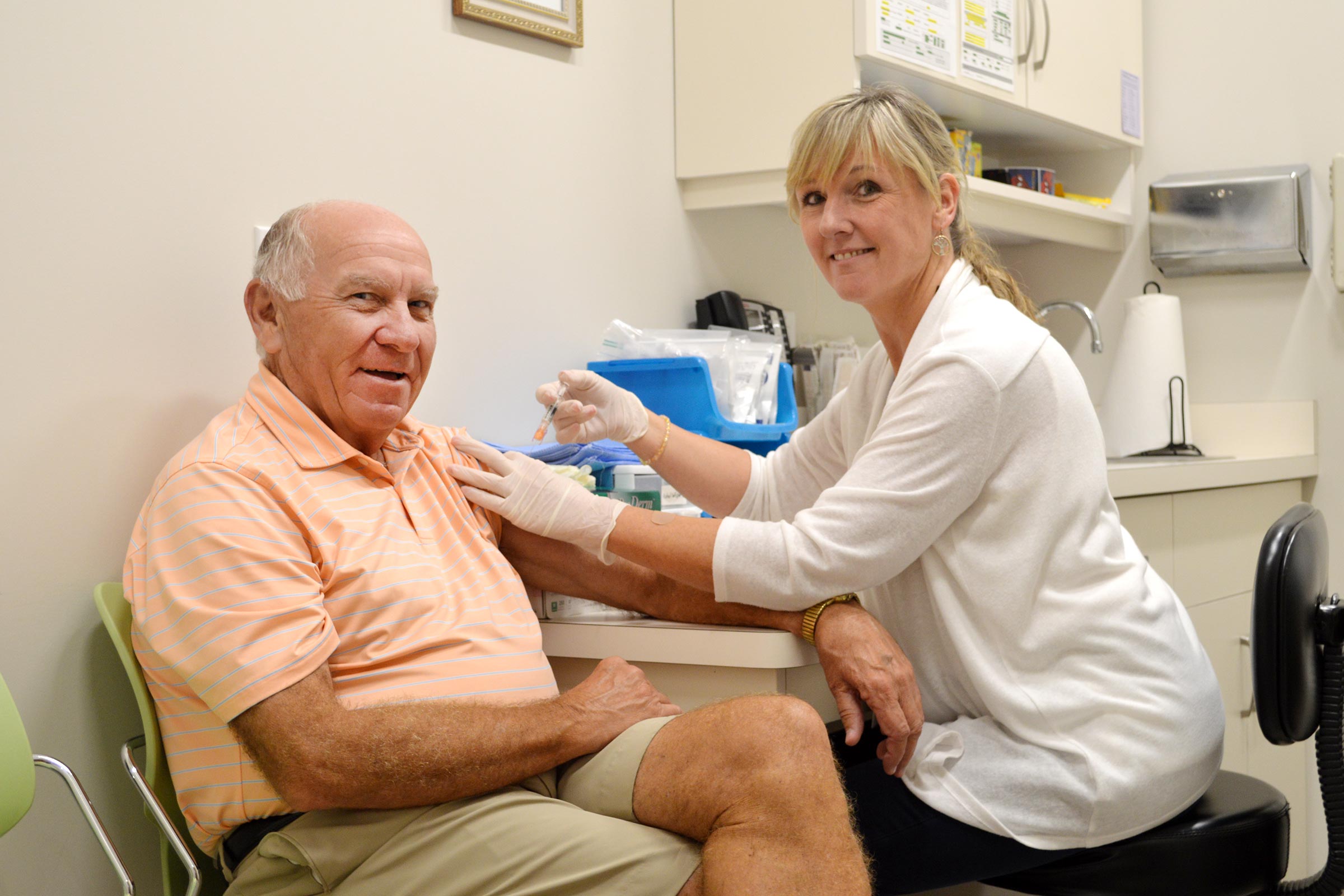 A middle aged man wearing a peach-colored shirt gets his flu shot from a blonde nurse wearing a white jacket