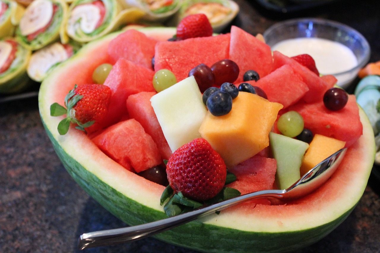 Fruit salad nestled in a watermelon bowl, with a platter of wraps in the background.