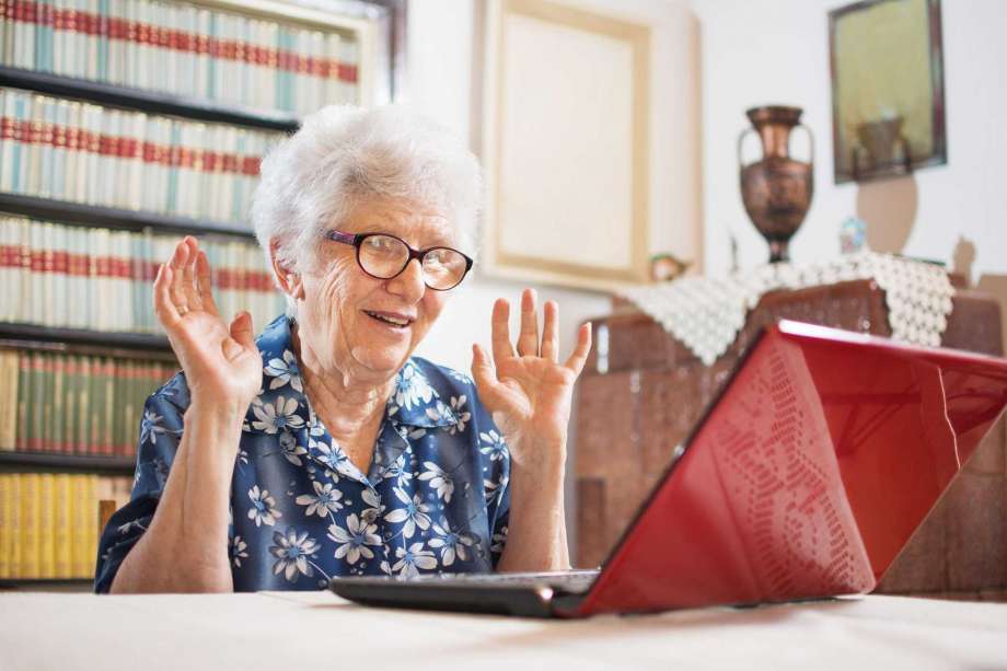 A senior woman looks delighted to see a message from a loved one appear on her laptop.