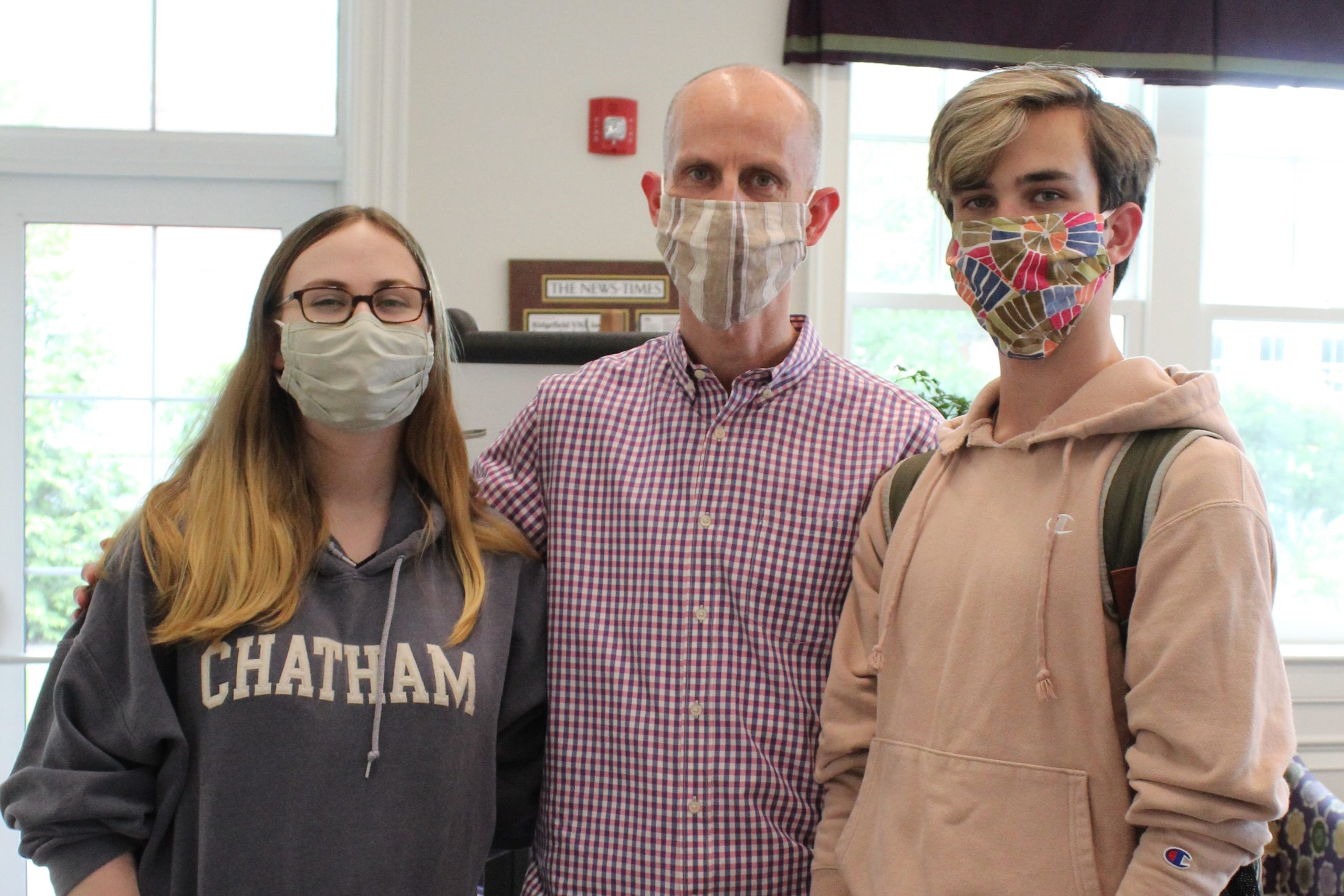 A teenage girl wearing a sweatshirt and glasses, her brother wearing a sweatshirt, and their father, all wearing masks, pose for a photo before getting their flu shots