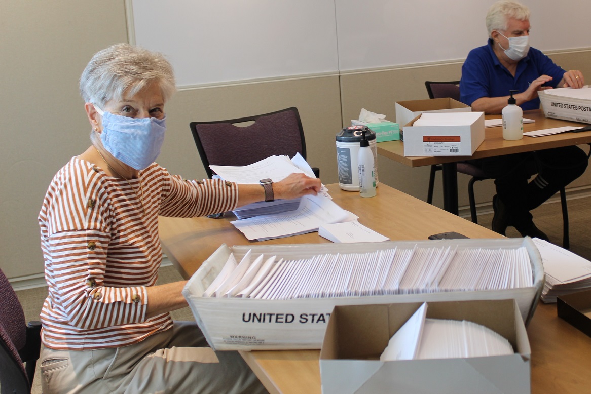 A smiling female volunteer wearing a surgical mask stuffs envelopes at RVNAhealth