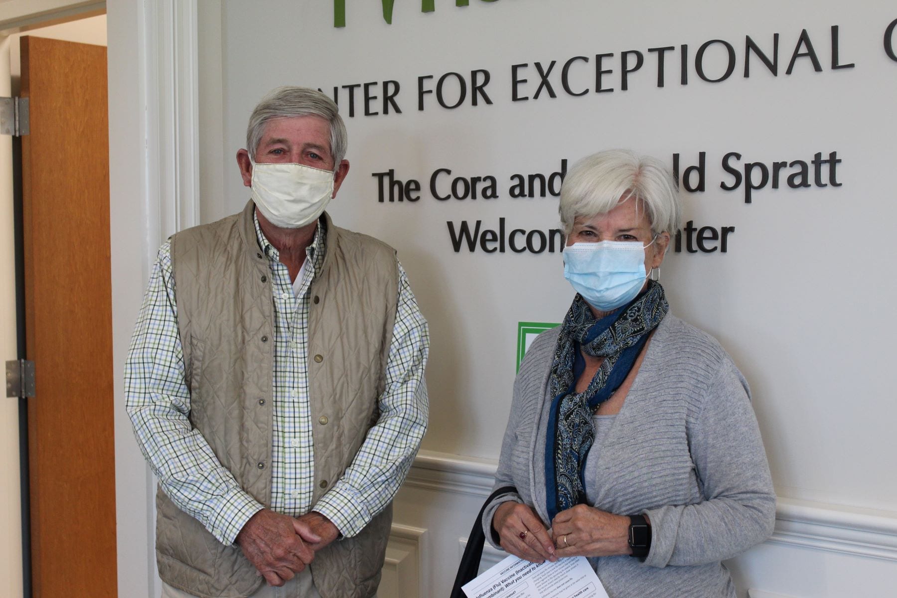 A man wearing a tan vest and a woman wearing a blue scarf await their flu shots in the RVNAhealth lobby